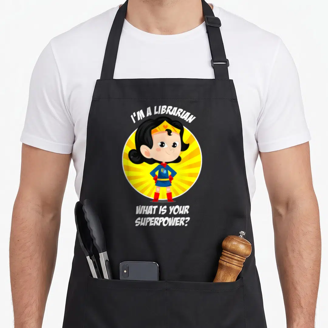 Superpower librarian apron - Cartoon superhero girl in front of yellow sunburst with white text reading I'M A LIBRARIAN — shown on a black cotton canvas apron against a white background