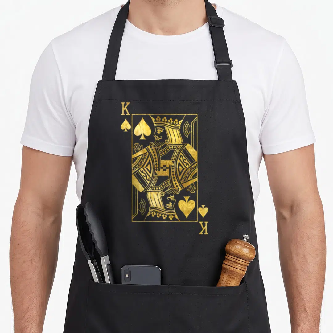 Lucky king apron - Gold King of Spades playing card with K corners and spade symbols — shown on a black cotton canvas apron against a white background