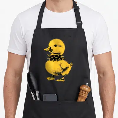 Rocker punk rock apron - Yellow cartoon duckling wearing a black spiked collar — shown on a black cotton canvas apron against a white background