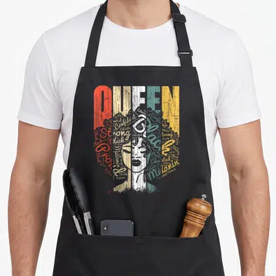 Queen african print apron - QUEEN text with woman's face formed by words strong confident melanin in red beige white — shown on a black cotton canvas apron against a white background