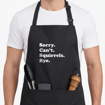 Retro squirrel aprons - White text reading Sorry Can't Squirrels Bye stacked vertically — shown on a black cotton canvas apron against a white background