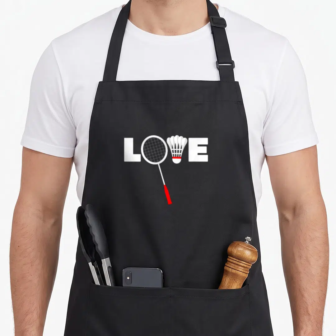 Cute badminton apron - LOVE text with racket replacing O and shuttlecock replacing V in white and red — shown on a black cotton canvas apron against a white background