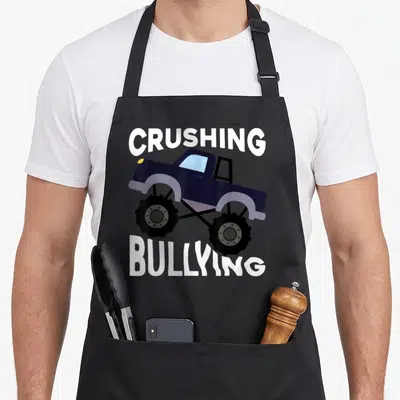 Unity truck apron - Dark blue monster truck with white text crushing bullying pun — shown on a black cotton canvas apron against a white background