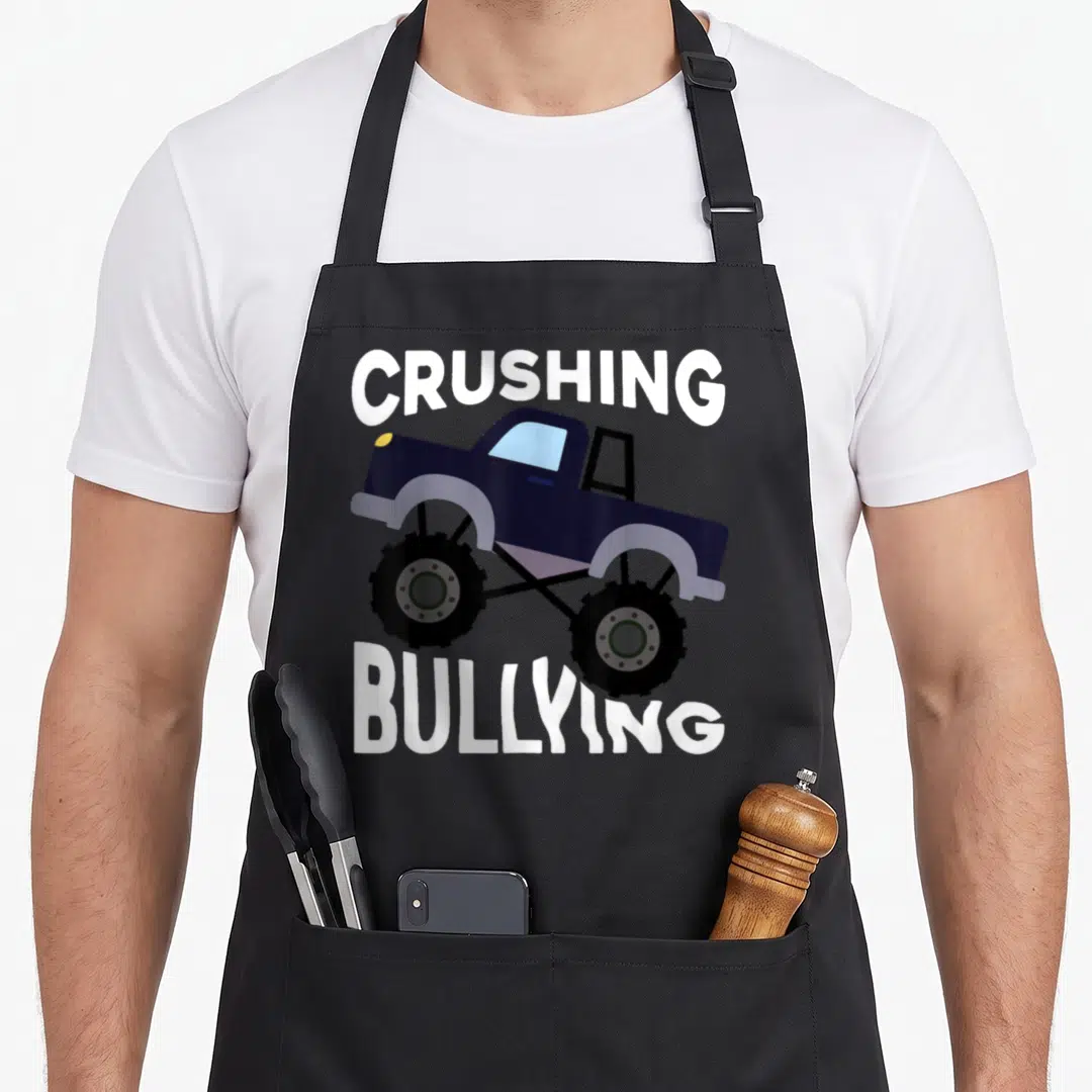 Unity truck apron - Dark blue monster truck with white text crushing bullying pun — shown on a black cotton canvas apron against a white background