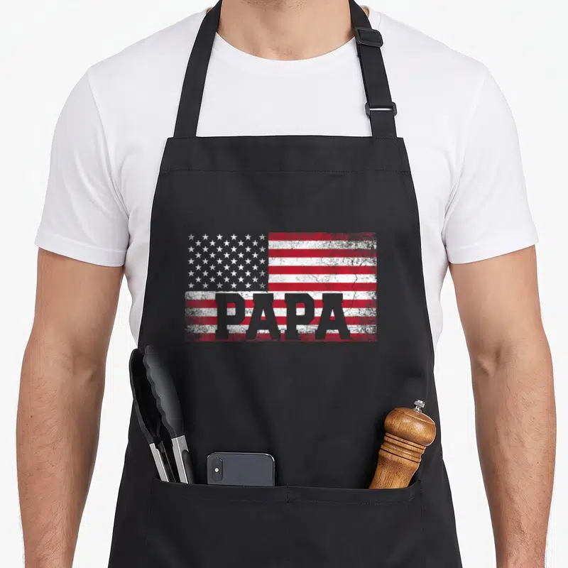 July father day apron - Distressed American flag in red white and grey with PAPA text overlaid — shown on a black cotton canvas apron against a white background