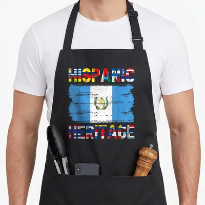 Hispanic guatemalan aprons - HISPANIC HERITAGE text framing a distressed Guatemalan flag with multi-colored letter fills — shown on a black cotton canvas apron against a white background