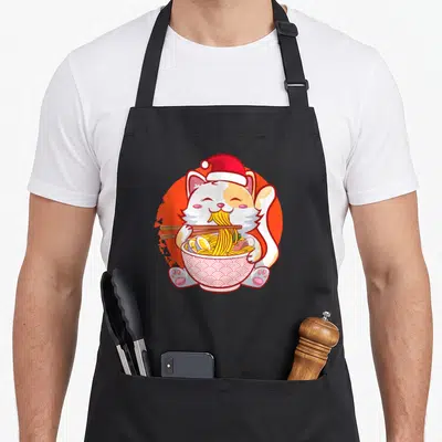 Ramen anime mom apron - Cartoon cat in Santa hat eating ramen noodles with chopsticks on orange circle — shown on a black cotton canvas apron against a white background
