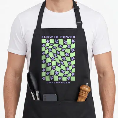 Danish pastel aprons - Retro warped checkerboard light green purple squares with flowers and FLOWER POWER COPENHAGEN — shown on a black cotton canvas apron against a white background
