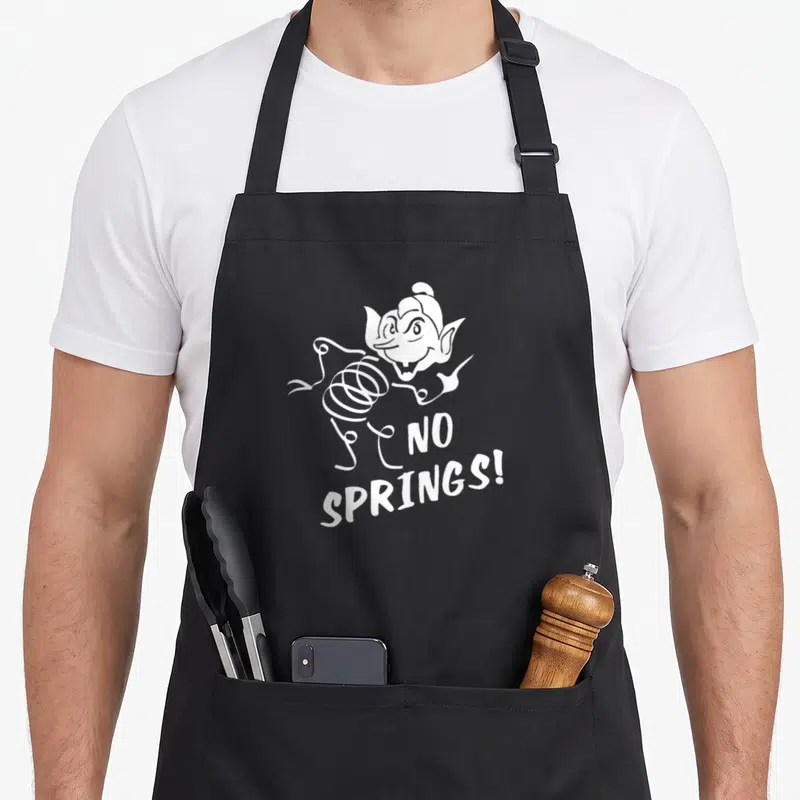 Coily science apron - White cartoon creature with spring body and no springs text — shown on a black cotton canvas apron against a white background