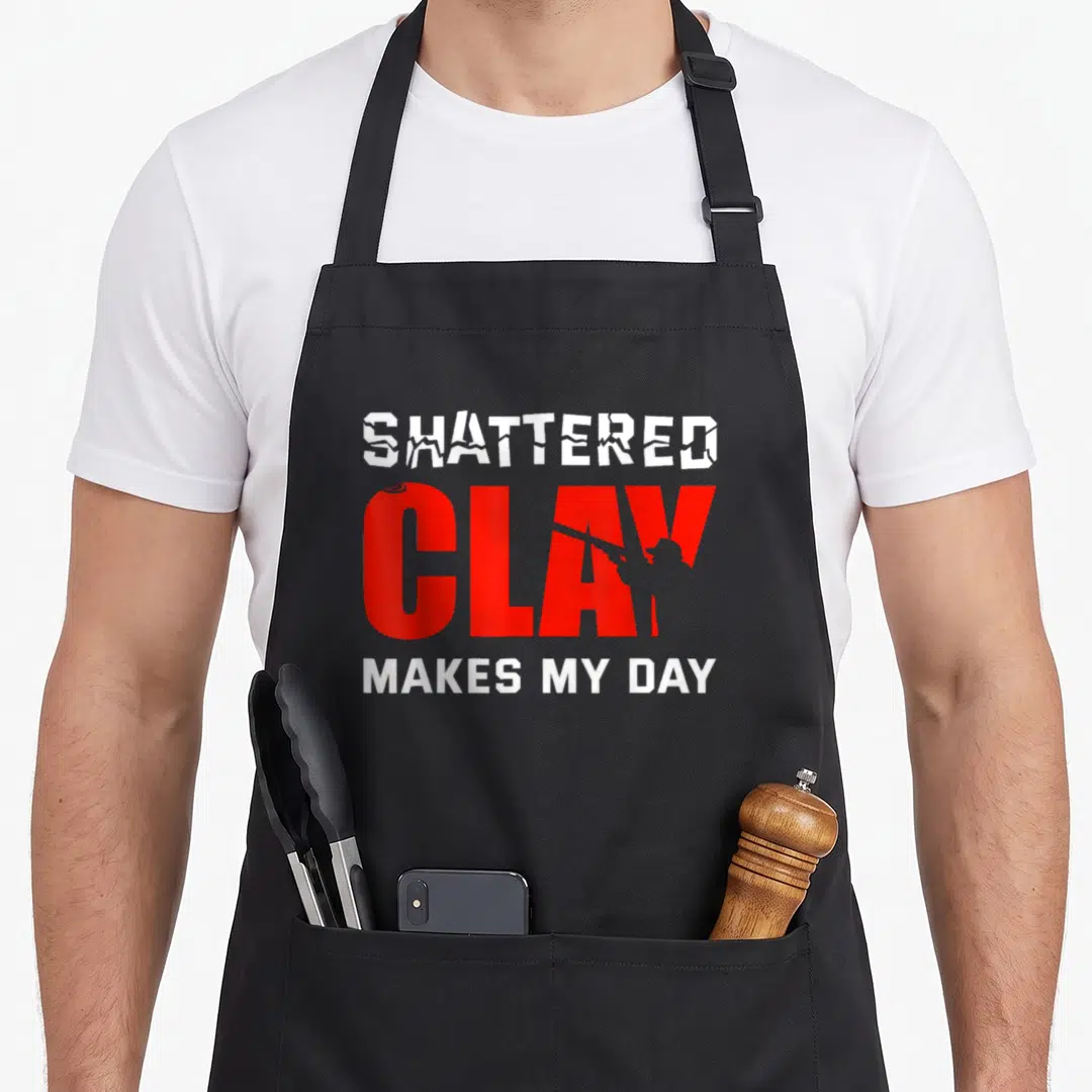Shattered clay apron - Red and white text SHATTERED CLAY MAKES MY DAY with grey shooter silhouette inside the lettering — shown on a black cotton canvas apron against a white background