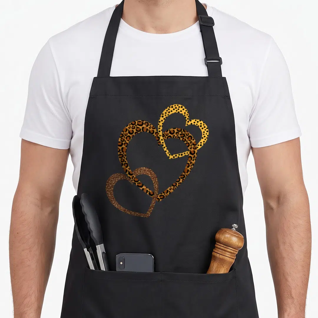Cheetah leopard print apron - Three overlapping leopard print hearts in brown, tan, black, and yellow minimalist design — shown on a black cotton canvas apron against a white background