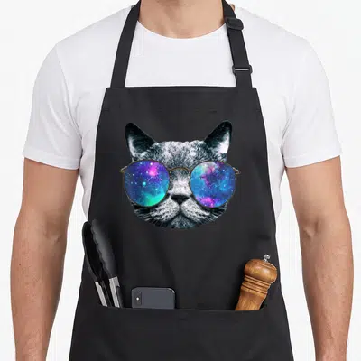 Glass space cat apron - Grey cat head wearing round gold sunglasses reflecting a blue purple and gold galaxy — shown on a black cotton canvas apron against a white background