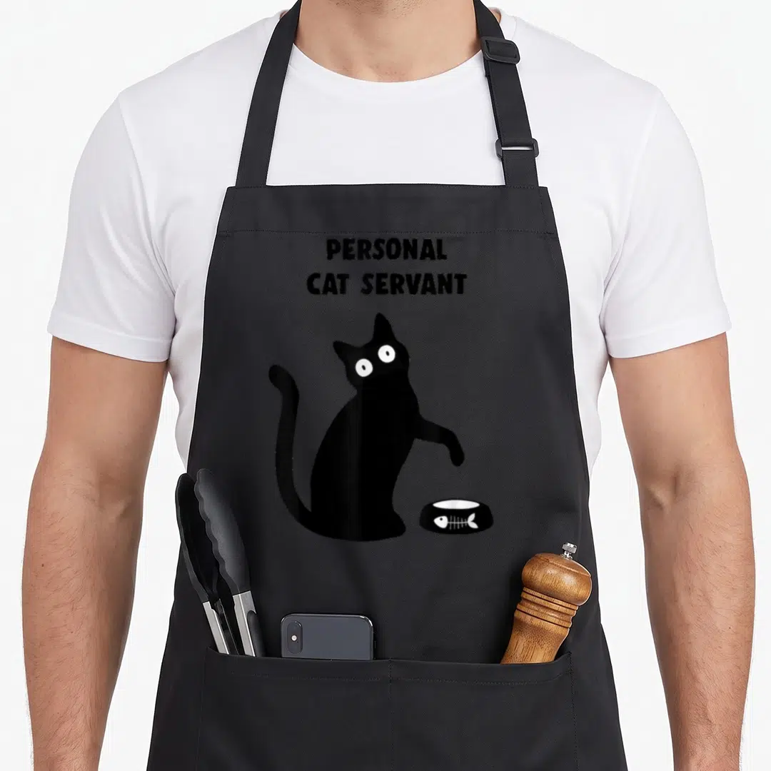 Servant personal apron - Black cat silhouette beside empty fish skeleton bowl with stacked text — shown on a black cotton canvas apron against a white background