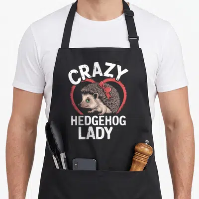Cute animal crazy hedgehog lady apron - CRAZY HEDGEHOG LADY text with brown hedgehog in red heart — shown on a black cotton canvas apron against a white background