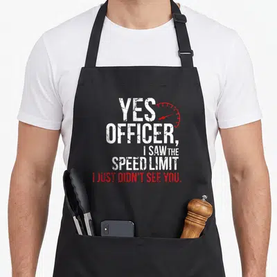 Officer mechanic apron - Distressed white text Yes Officer I Saw Speed Limit with red speedometer arc — shown on a black cotton canvas apron against a white background