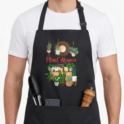 Mama plant lady apron - Plant Mama text above three hanging plants and shelf with potted greenery — shown on a black cotton canvas apron against a white background