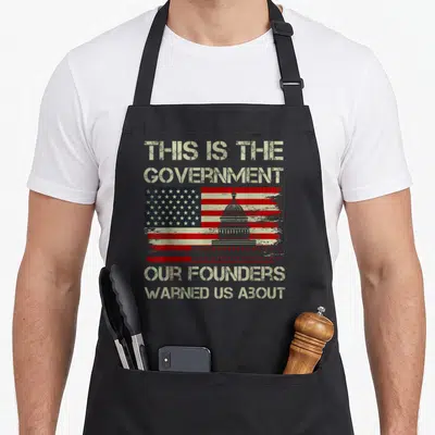 Our us aprons - US Capitol building over distressed flag with beige stenciled text reading 'This Is The Government Our — shown on a black cotton canvas apron against a white background