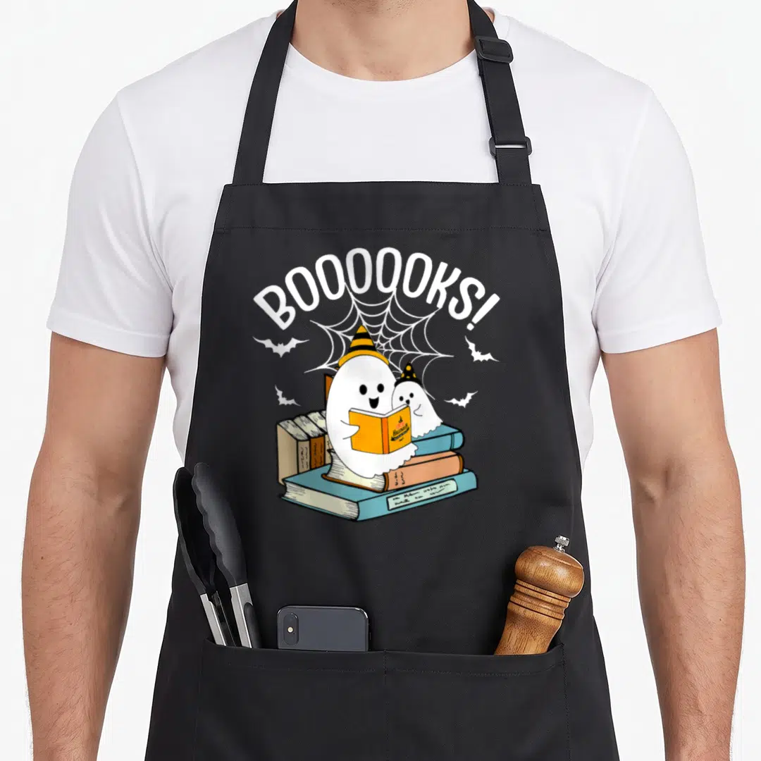 Booook ghost halloween apron - Two cartoon ghosts in witch hats reading books under arched BOOOOOKS! text and spider web — shown on a black cotton canvas apron against a white background