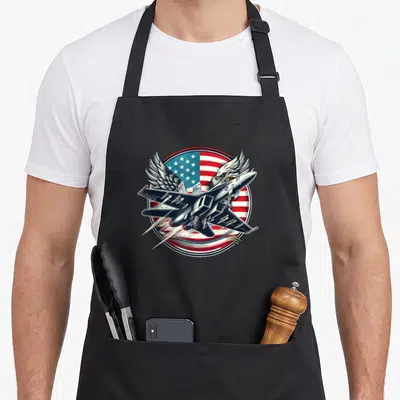 Fighter aviation apron - Cartoon fighter jet over US flag with eagle wings emerging from behind in red white and blue — shown on a black cotton canvas apron against a white background