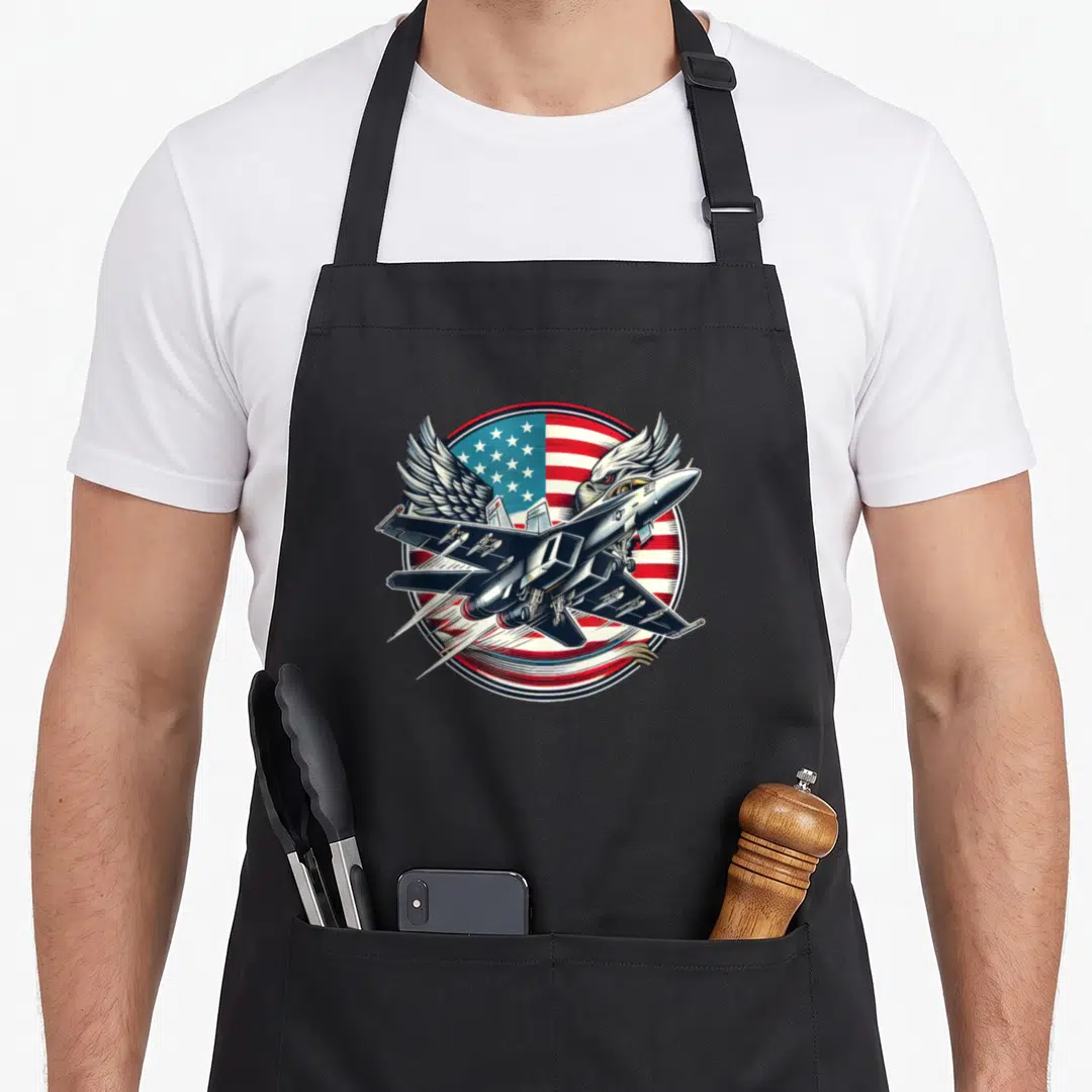 Fighter aviation apron - Cartoon fighter jet over US flag with eagle wings emerging from behind in red white and blue — shown on a black cotton canvas apron against a white background