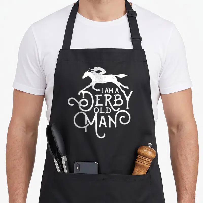Derby kentucky horse apron - White distressed horse and rider silhouette above stacked text I AM A DERBY OLD MAN — shown on a black cotton canvas apron against a white background