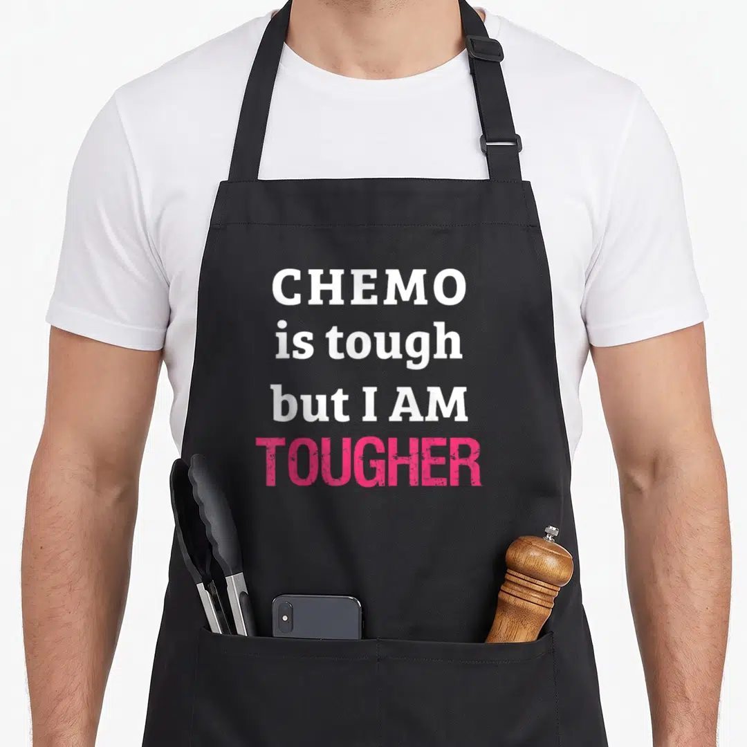Chemo beat apron - Stacked white and pink text reading CHEMO is tough but I AM TOUGHER — shown on a black cotton canvas apron against a white background
