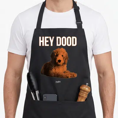 Funny goldendoodle apron - HEY DOOD text above realistic orange brown dog illustration — shown on a black cotton canvas apron against a white background