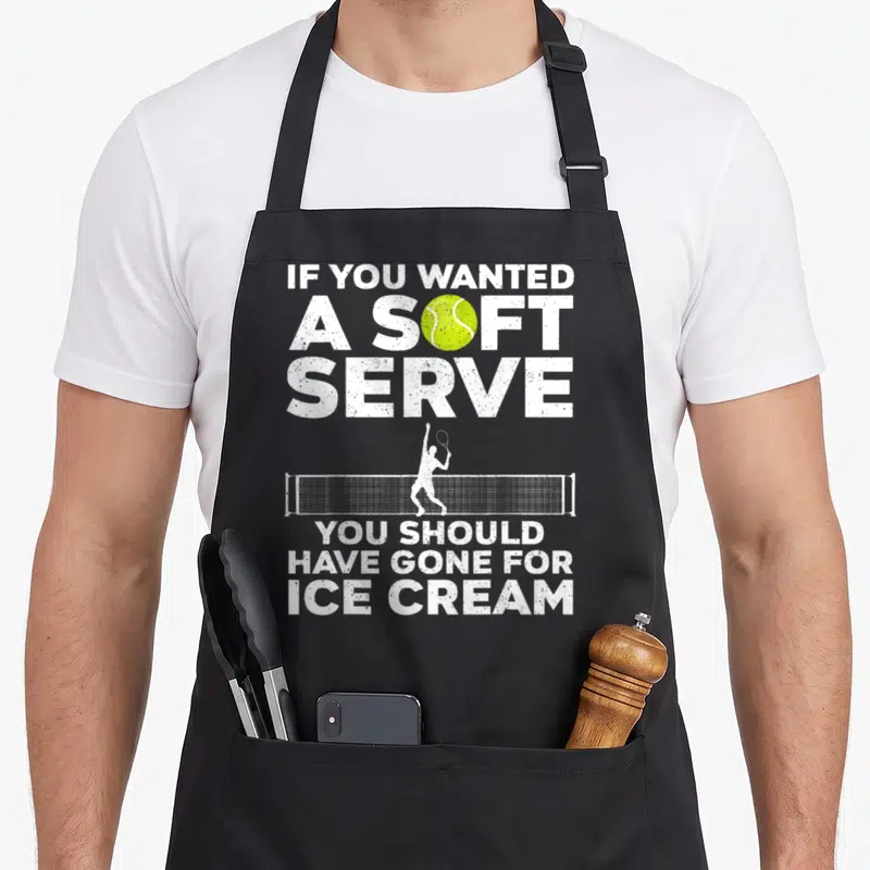 Funny player tennis apron - Tennis player silhouette hitting ball over net with white distressed text and yellow-green — shown on a black cotton canvas apron against a white background