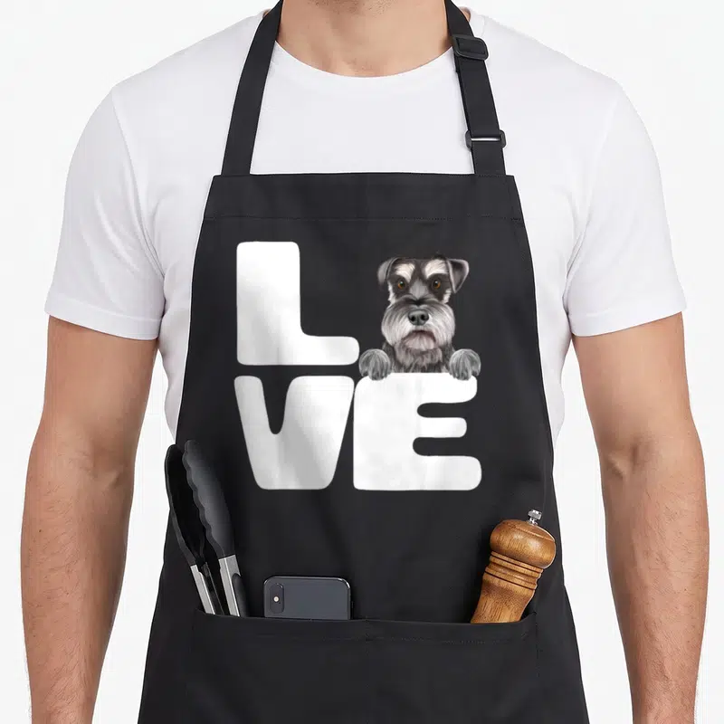Cool dog miniature schnauzer apron - Realistic grey and white dog peeking over white LOVE letters — shown on a black cotton canvas apron against a white background