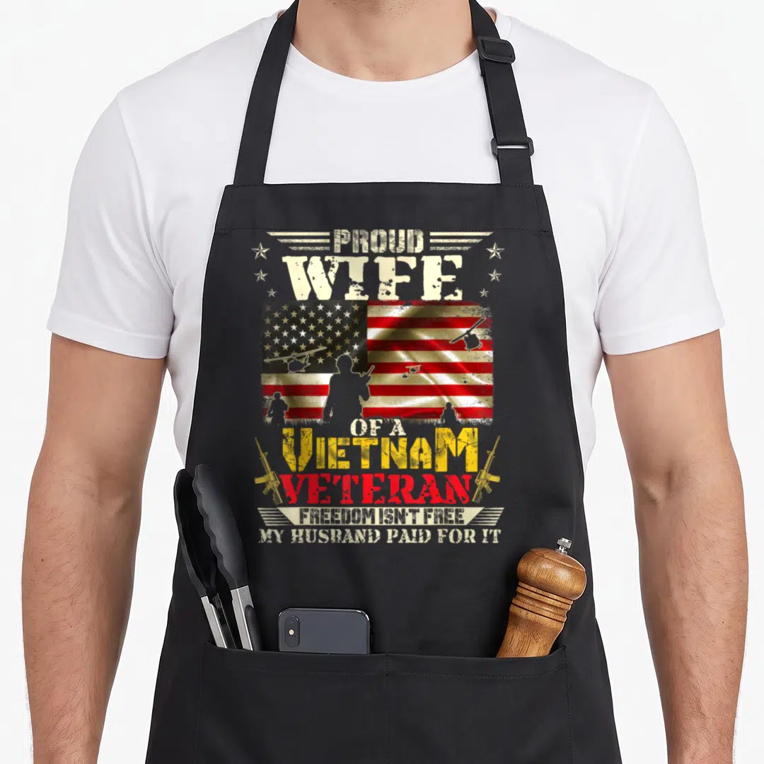 Freedom best husband apron - Distressed USA flag with soldier silhouettes and text Proud Wife of a Vietnam Veteran — shown on a black cotton canvas apron against a white background