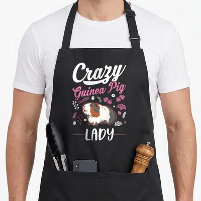 Vintage animal crazy guinea lady apron - Cartoon guinea pig with Crazy Guinea Pig LADY text and white pink floral — shown on a black cotton canvas apron against a white background