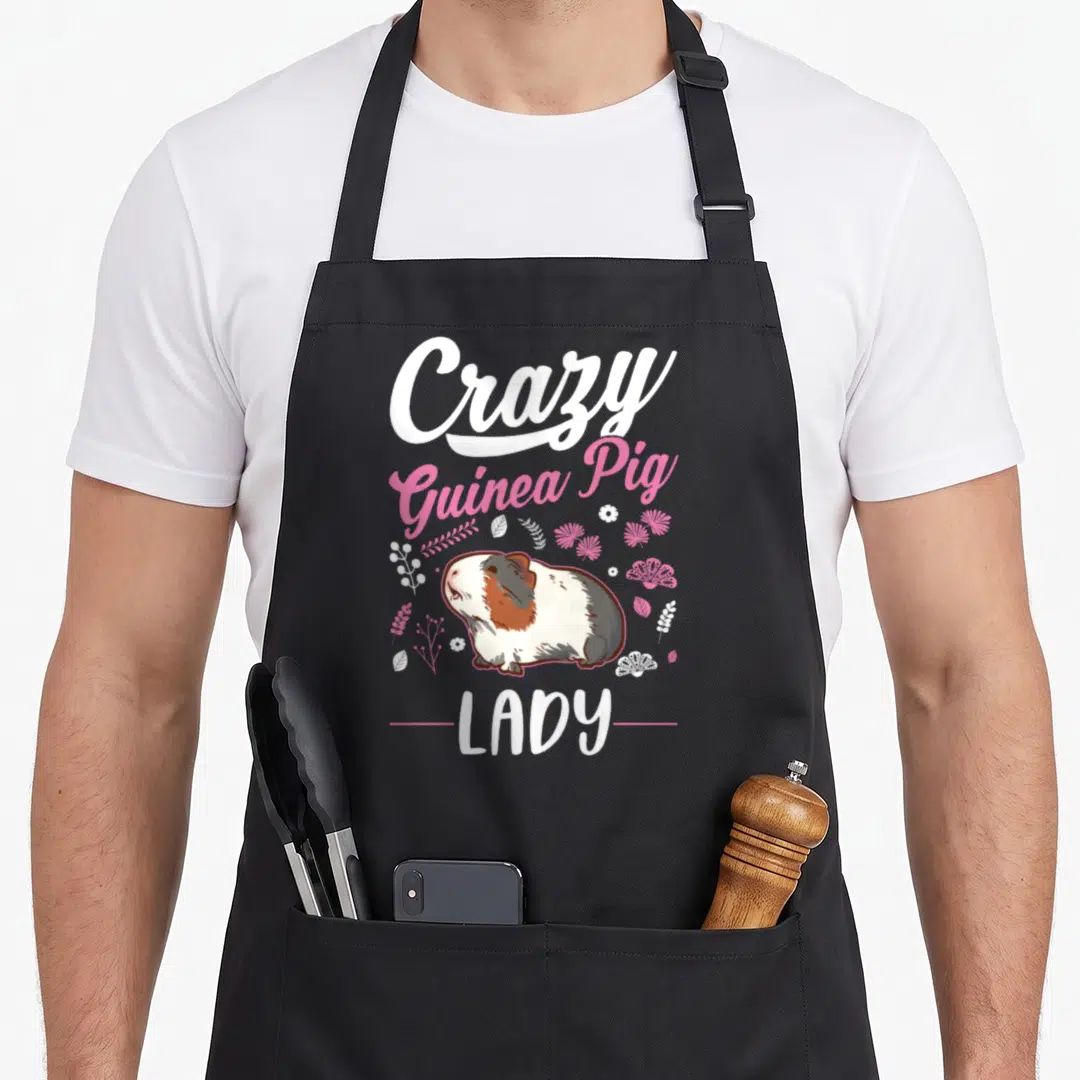 Vintage animal crazy guinea lady apron - Cartoon guinea pig with Crazy Guinea Pig LADY text and white pink floral — shown on a black cotton canvas apron against a white background