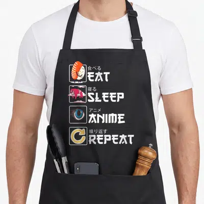 Kawaii sushi apron - Four square icons showing shrimp, sleep, eye, repeat with Japanese and English text — shown on a black cotton canvas apron against a white background