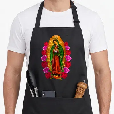 Virgen mary apron - Our Lady of Guadalupe in golden mandorla surrounded by red and pink roses with small angel — shown on a black cotton canvas apron against a white background