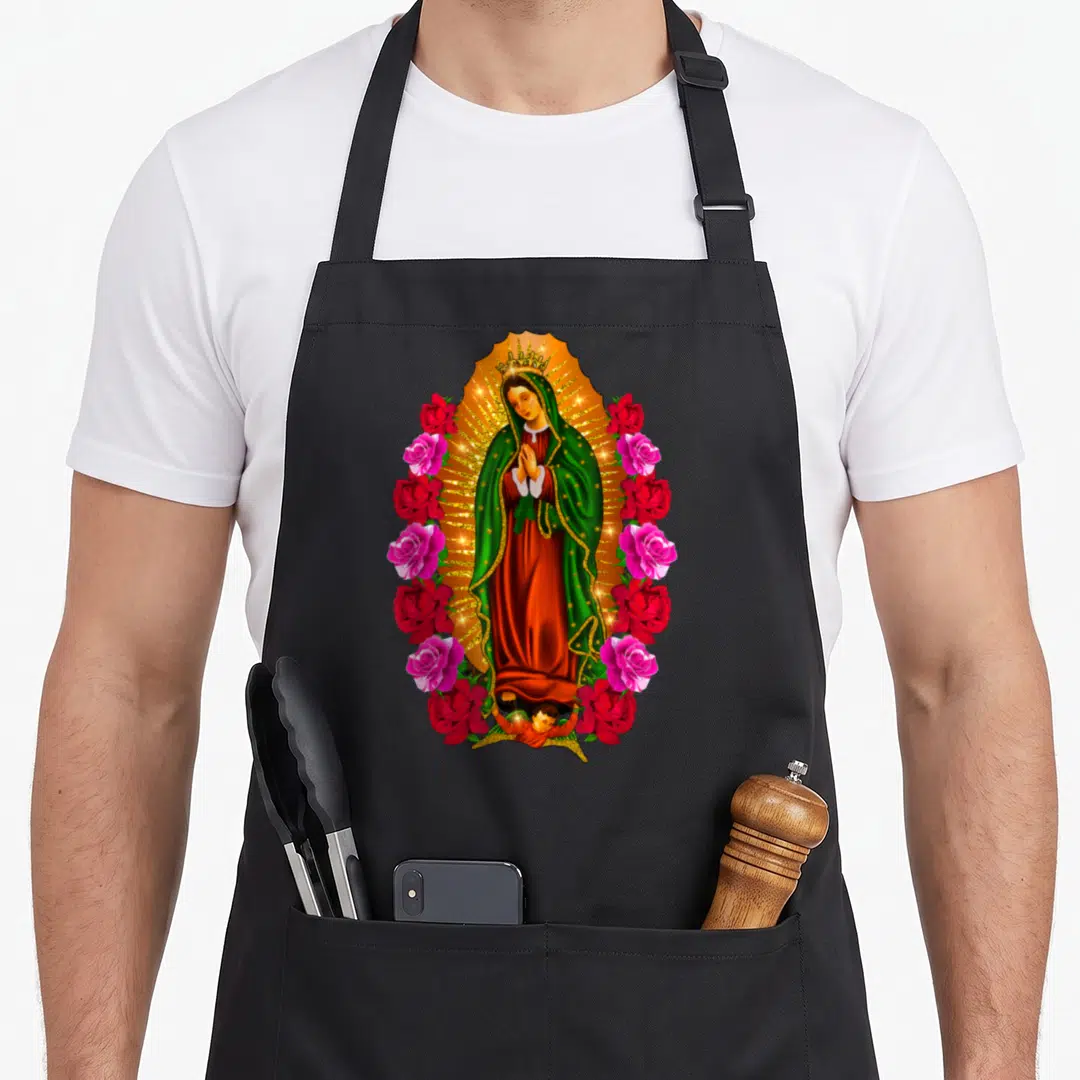 Virgen mary apron - Our Lady of Guadalupe in golden mandorla surrounded by red and pink roses with small angel — shown on a black cotton canvas apron against a white background