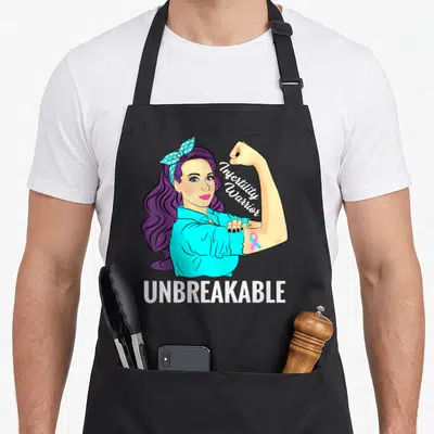 Warrior infertility awareness apron - Cartoon woman flexing arm with Infertility Warrior text and pink cyan ribbon — shown on a black cotton canvas apron against a white background