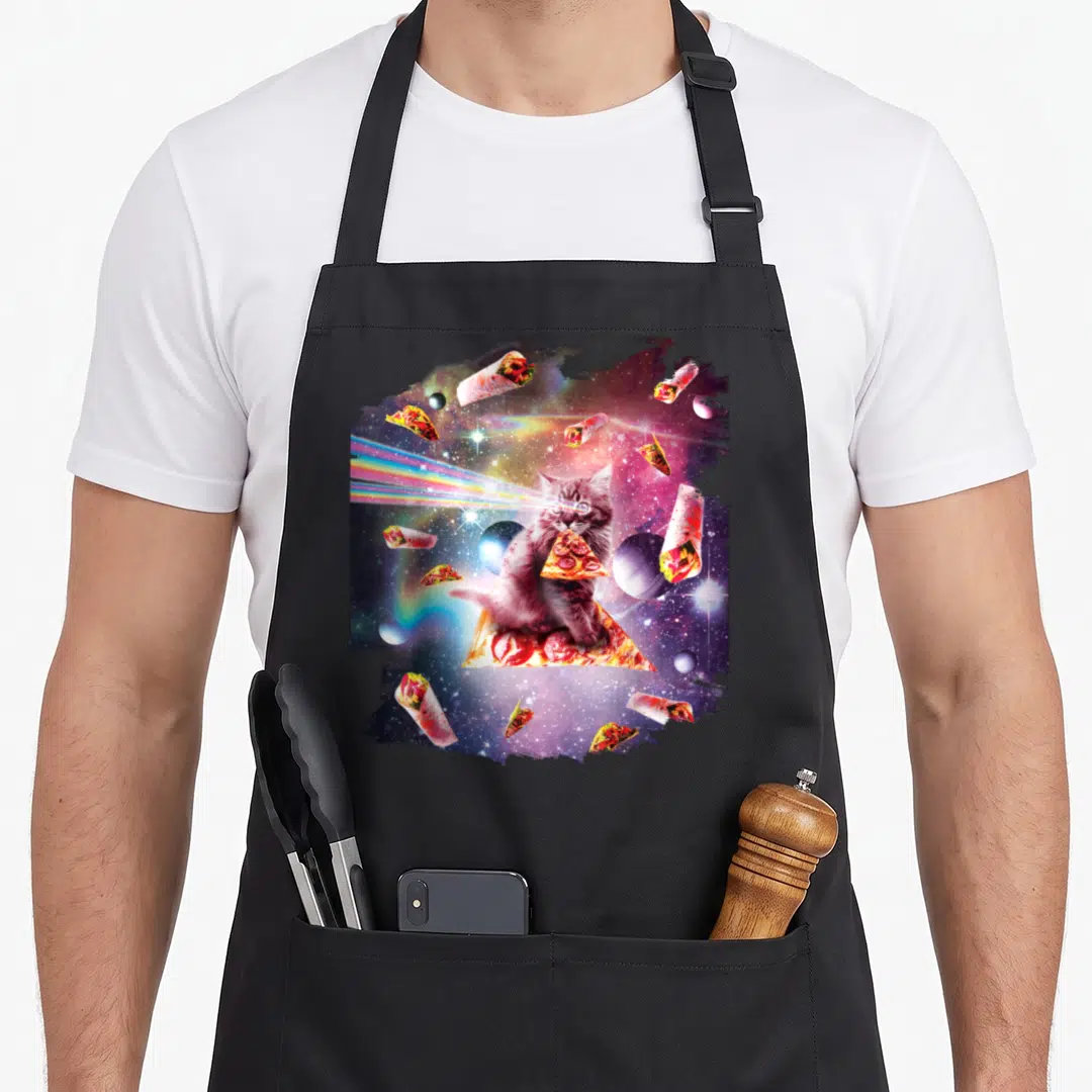 Outer space cat apron - Kitten on pizza slice with rainbow laser eyes surrounded by floating burritos and tacos — shown on a black cotton canvas apron against a white background