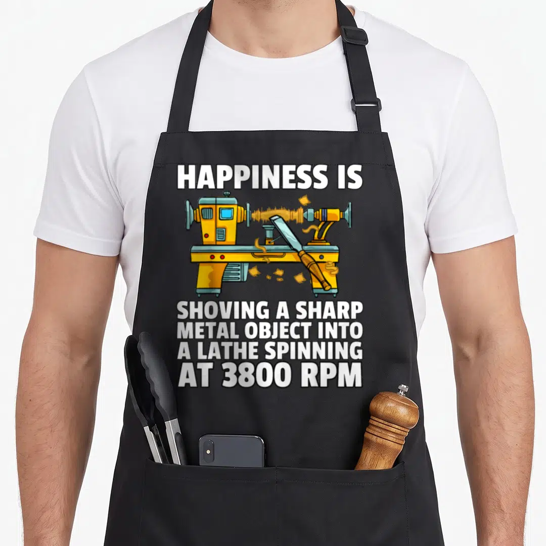 Woodturning woodworker's apron - Cartoon yellow lathe with chisel and white text about 3800 RPM woodturning humor — shown on a black cotton canvas apron against a white background