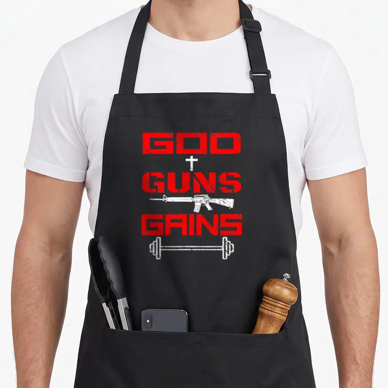God friends apron - Red distressed text reading God Guns Gains with white cross, rifle, and barbell icons stacked — shown on a black cotton canvas apron against a white background