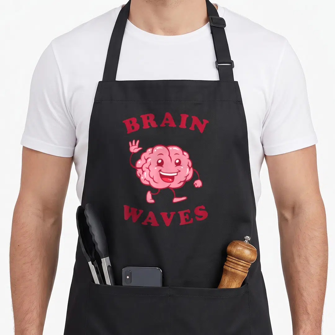 Wave science apron - Pink cartoon brain character waving between red BRAIN WAVES text — shown on a black cotton canvas apron against a white background
