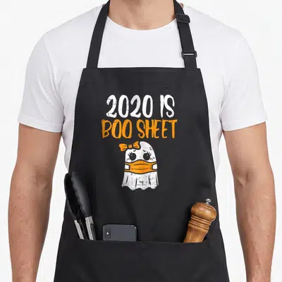 Quarantine halloween apron - 2020 IS BOO SHEET text above masked white ghost with orange bow — shown on a black cotton canvas apron against a white background