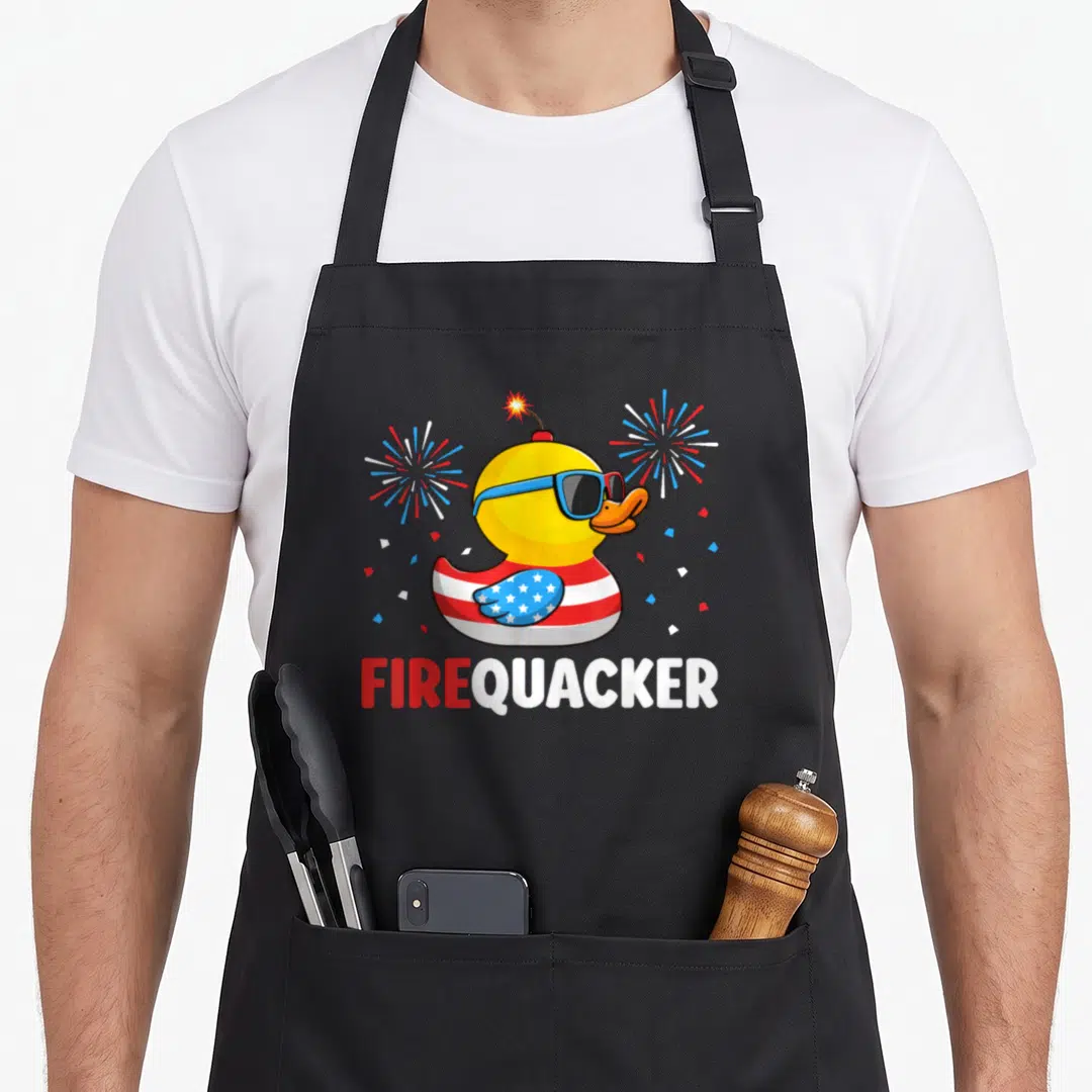 Duck 4th of july apron - Yellow rubber duck with sunglasses and FIREQUACKER text surrounded by red white and blue — shown on a black cotton canvas apron against a white background