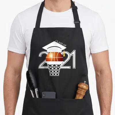 Graduation class player apron - Basketball inside hoop with graduation cap and CLASS OF 2021 text in white orange — shown on a black cotton canvas apron against a white background