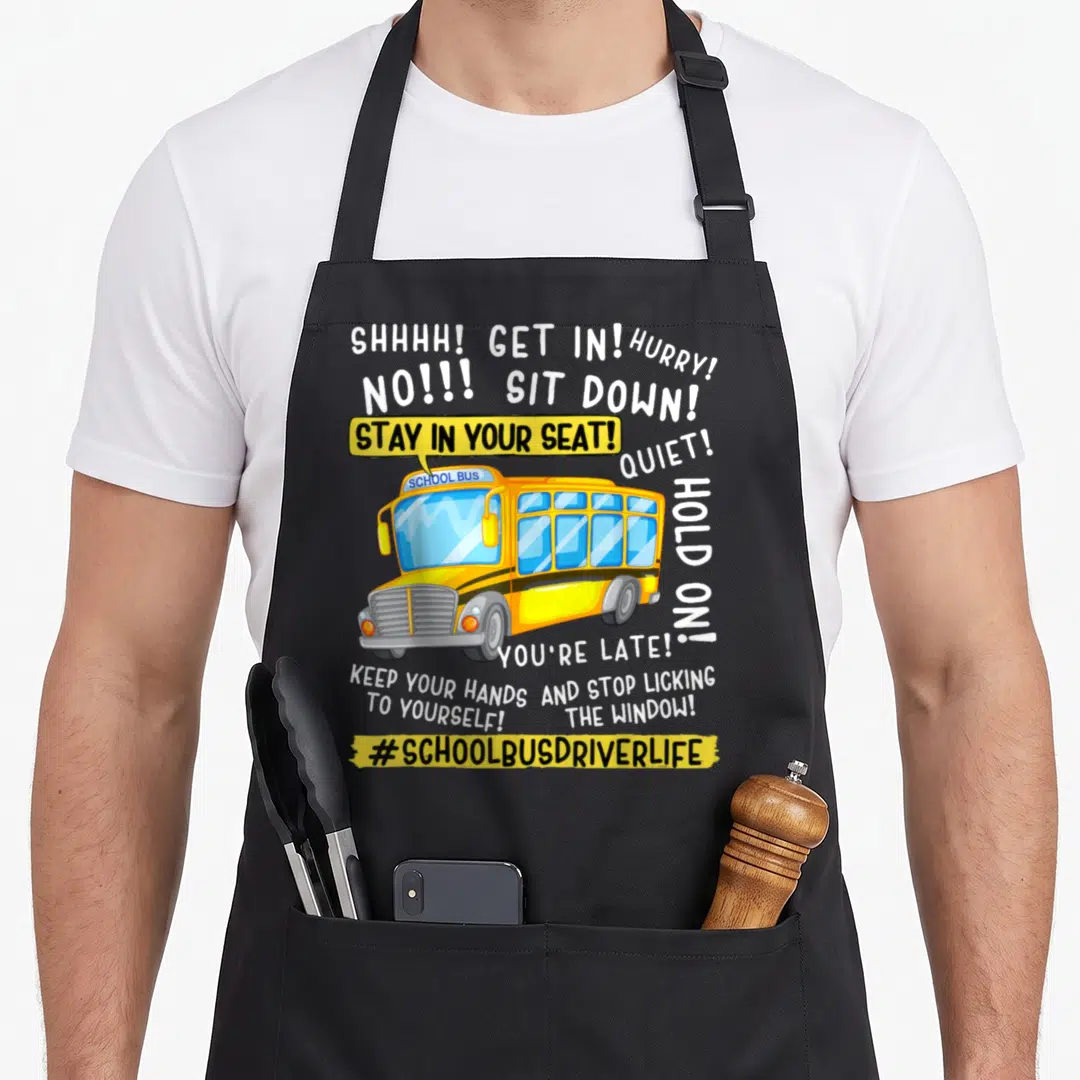 Bus teacher apron - Cartoon yellow bus with white text commands like STAY IN YOUR SEAT and KEEP YOUR HANDS TO YOURSELF — shown on a black cotton canvas apron against a white background
