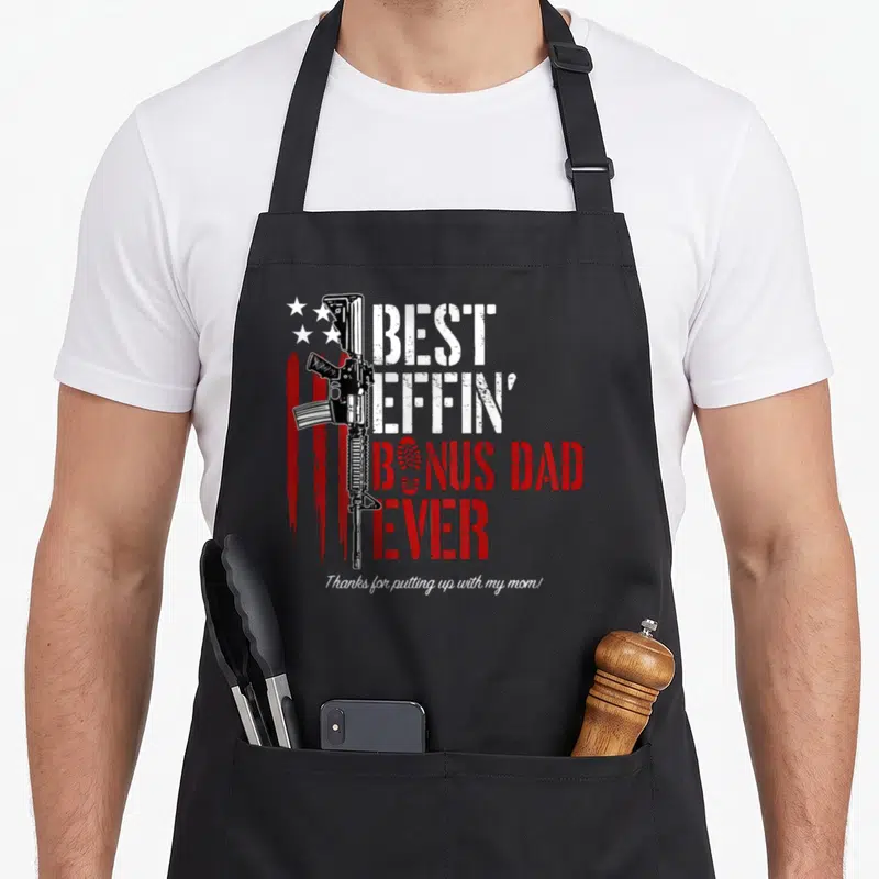 Effin novelty apron - Vertical rifle next to stacked text BEST EFFIN BONUS DAD EVER with red stripes and stars — shown on a black cotton canvas apron against a white background