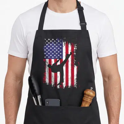 Funny taekwondo karate apron - Grey martial artist silhouette kicking in front of a distressed red white and blue USA — shown on a black cotton canvas apron against a white background