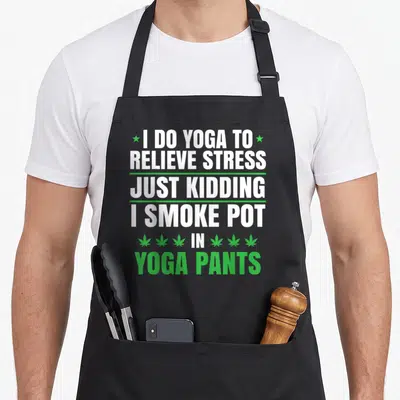 Smoke i love smoking apron - Stacked white and green text reading I DO YOGA TO RELIEVE STRESS with six cannabis leaves — shown on a black cotton canvas apron against a white background