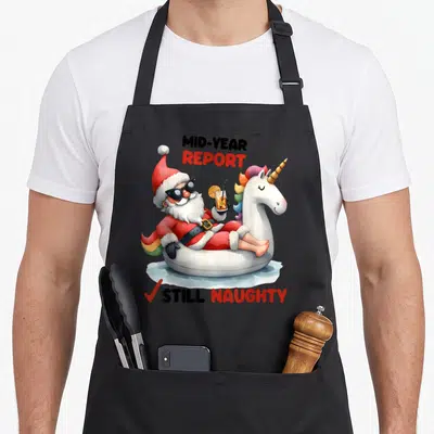 Pool christmas santa apron - Santa in sunglasses on unicorn floatie holding drink with mid-year report still naughty — shown on a black cotton canvas apron against a white background