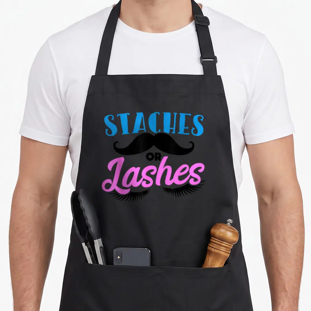 Stach apron or apron - STACHES OR Lashes text with black mustache and pink eyelashes graphic — shown on a black cotton canvas apron against a white background