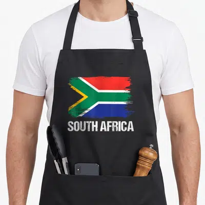 Pride south african apron - Distressed South African flag in red green blue yellow white above white text SOUTH AFRICA — shown on a black cotton canvas apron against a white background